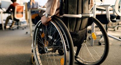 Im Hintergrund schemenhaft Veranstaltungsraum, im Vordergrund ein Rollstuhlfahrer von hinten