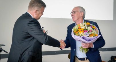 Herr Heidmeier schüttelt Wolfgang Schmitz die Hand, Wolfgang Schmitz mit überreichtem Blumenstrauß in der Hand