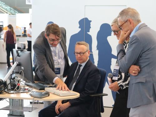 Dr. Benjamin Limbach wird der barrierefreie Computerarbeitsplatz durch Rainer Wallbruch (Agentur Barrierefrei NRW) gezeigt. Daneben stehen zwei weitere Personen und schauen zu.