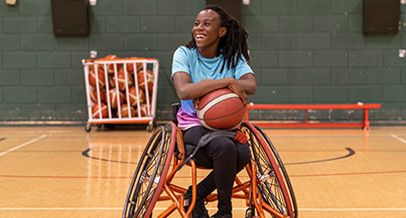 Schwarze Frau im Sport-Rollstuhl, die einen Basketball auf dem Schoß festhält