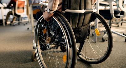 Im Hintergrund schemenhaft Veranstaltungsraum, im Vordergrund ein Rollstuhlfahrer von hinten