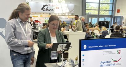 Besucherin spielt das Spiel auf einem Tablet am Messestand der Agentur, ein Mitarbeiter der Agentur begleitet dies