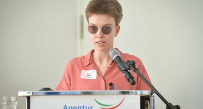Eine Frau mit getönter Brille am Rednerpult mit Mirkrofon
