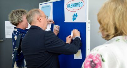 Herr Ohm und Frau Schiffers heften Glückwunschkarten an die Pinwand