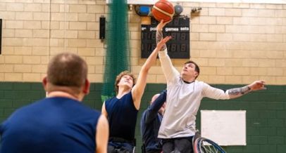 4 Personen im Rollstuhl spielen Basketball in einer Sporthalle