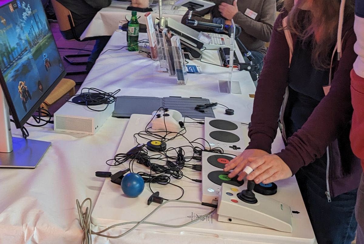 Foto zweier Personen die mit einem adaptiven Controller Set an einem Bildschirm spielen.