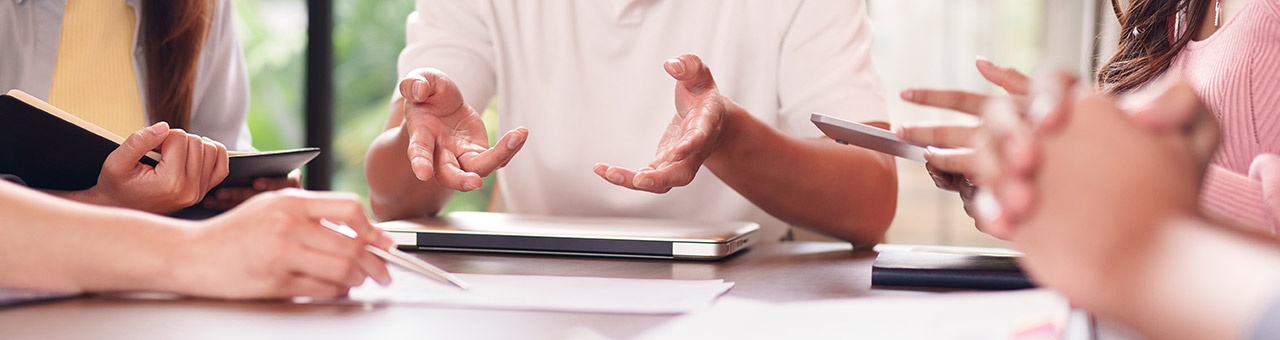 Mehrere Personen gestikulieren mit den Händen über einem Tisch während einer Besprechung