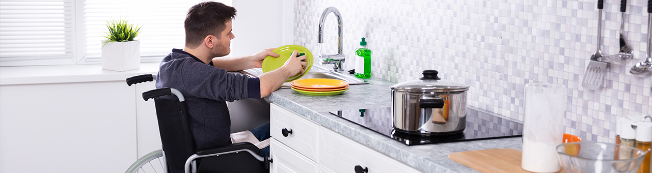 Mann im Rollstuhl beim Abwaschen von Geschirr in der Küche