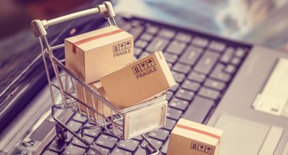 Mit Paketen gefüllter Miniatur-Einkaufswagen, der auf einer Laptop-Tastatur steht.